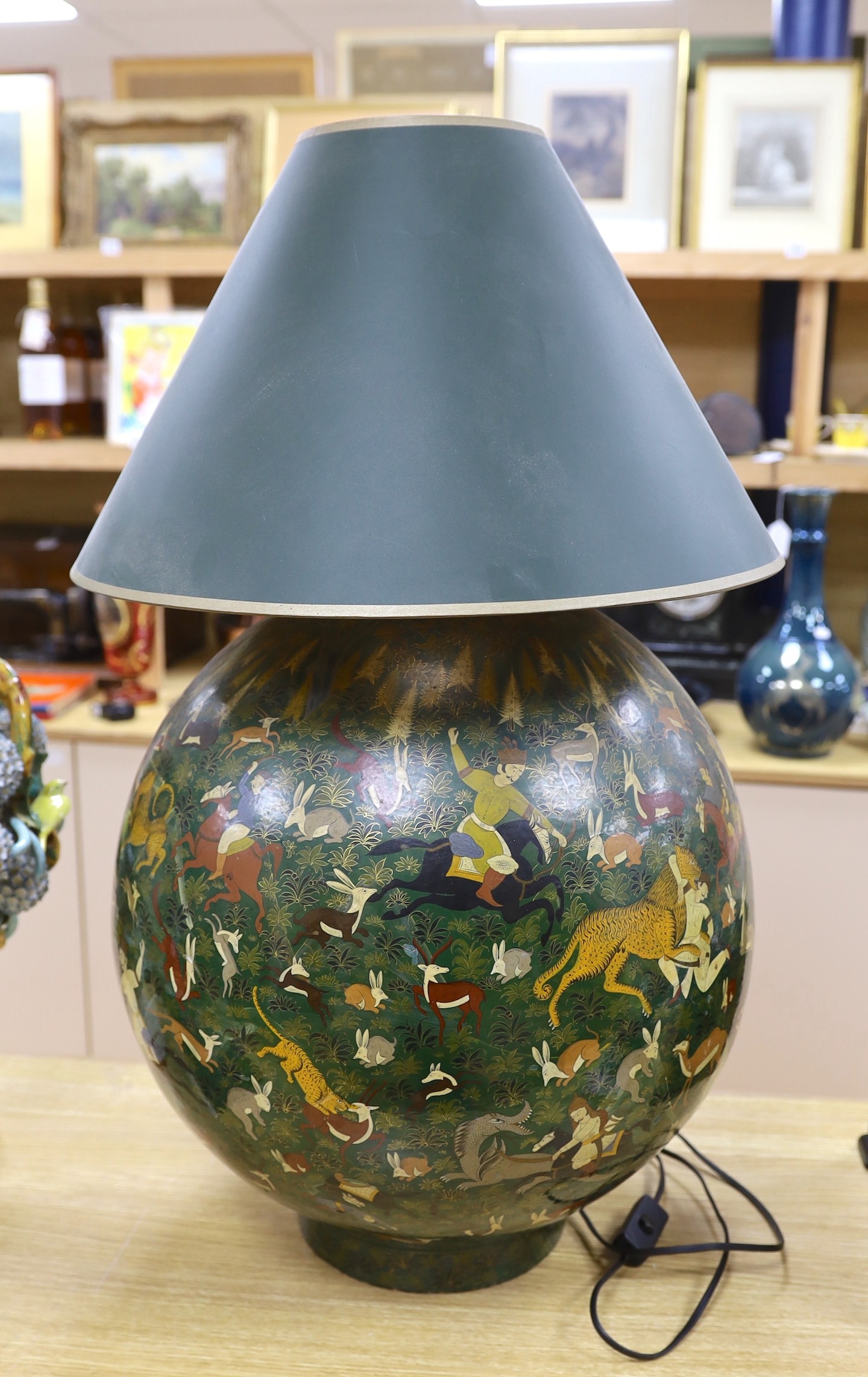 An Indian spherical green ground papier mache table lamp, decorated with hunting scenes and green shade, 75cms high including shade